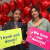 Two students hold up signs saying thank you donor and we love our donors and stand in front of red heart balloons