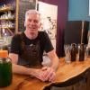 Dave Paul, owner of Love Shack Libations, leans against a wooden counter. Beer bottles and a glass is on his right.