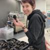 Melanie P. Loureiro stands in front of several bins of mussels and holds onel in her left hand.