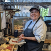 VIU Culinary Arts student Darlene Charlie making a sandwich in the Birch Tree cafe kitchen and smiling at the camera