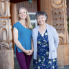VIU Psychedelic-assisted Therapy Program Chair Shannon Dames with VIU Elder-in-Residence C-tasi:a Geraldine Manson standing outside in front of totem poles and smiling at the camera