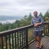 Stephen Hextall leans against a railing with trees and a lake in the background.